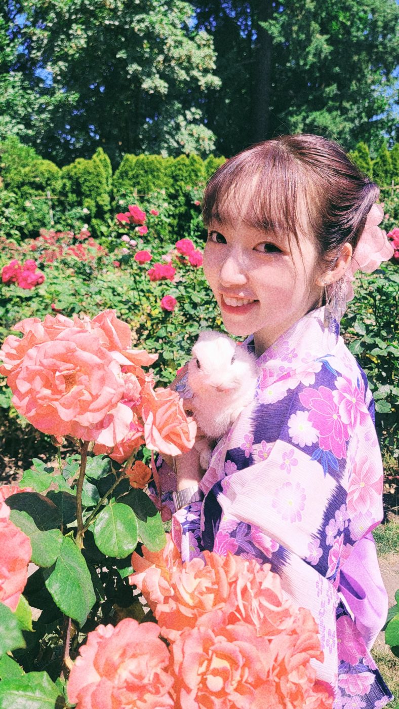 Jessie in a purple floral yukata holding her white rabbit Sato among pink roses